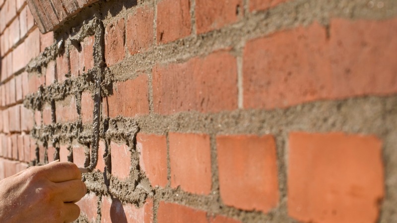 Workers carrying out repointing on exterior brick wall to repair damaged mortar joints