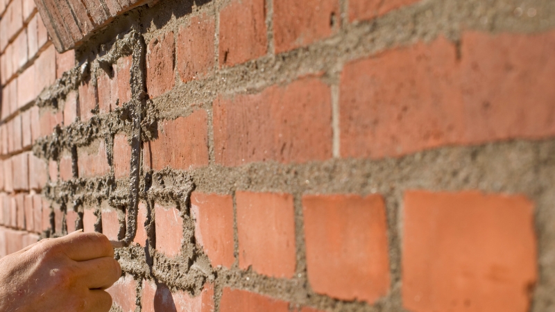 A close-up of a professional mason performing repointing on an old brick wall using lime mortar to restore structural integrity.